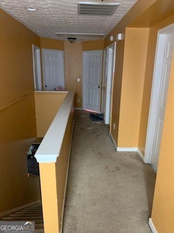 hallway featuring light colored carpet and a textured ceiling