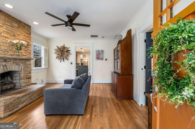 living room with crown molding, a stone fireplace, wood-type flooring, and ceiling fan