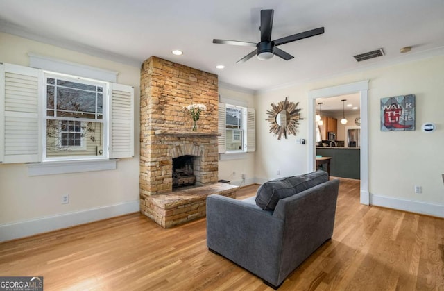 living room with a fireplace, crown molding, wood-type flooring, and ceiling fan