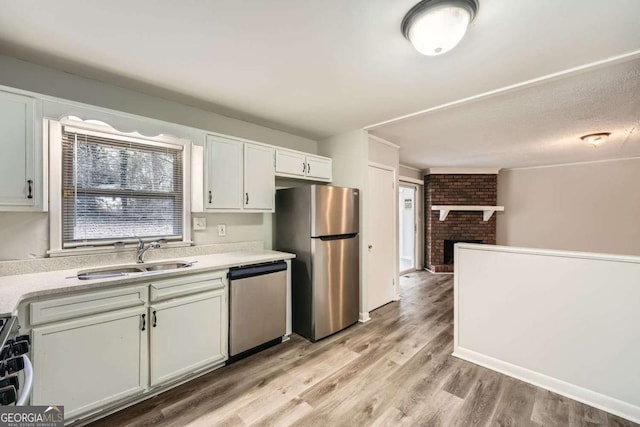 kitchen featuring appliances with stainless steel finishes, white cabinetry, sink, a brick fireplace, and light wood-type flooring