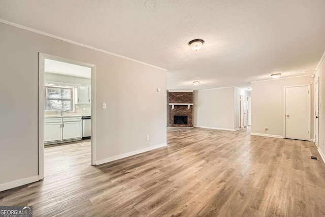 unfurnished living room with sink, ornamental molding, light hardwood / wood-style floors, a textured ceiling, and a brick fireplace