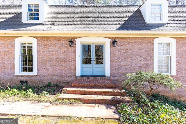 view of exterior entry featuring brick siding and roof with shingles