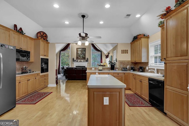 kitchen featuring vaulted ceiling, an island with sink, sink, light hardwood / wood-style floors, and black appliances