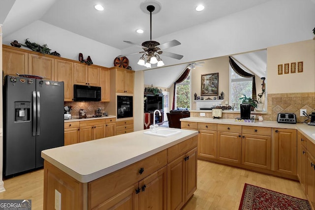 kitchen featuring sink, light hardwood / wood-style flooring, a center island, black appliances, and vaulted ceiling