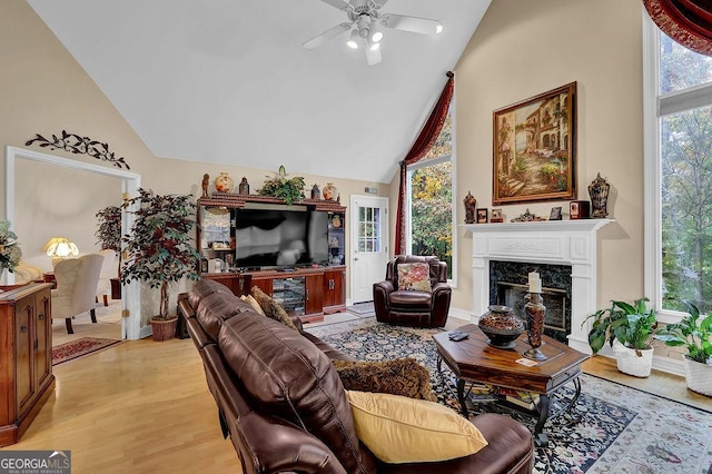 living room featuring ceiling fan, a high end fireplace, high vaulted ceiling, and light hardwood / wood-style floors