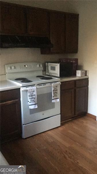 kitchen with dark brown cabinetry, dark hardwood / wood-style flooring, exhaust hood, and white appliances