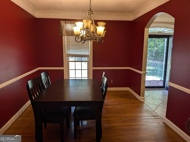 unfurnished dining area with a textured ceiling, wood-type flooring, ornamental molding, and a chandelier