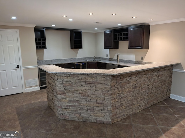 bar featuring sink, dark tile patterned floors, dark brown cabinetry, ornamental molding, and light stone countertops