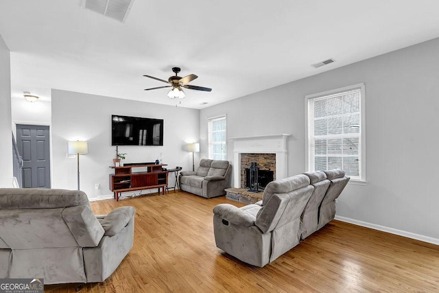 living room with ceiling fan, a stone fireplace, and light hardwood / wood-style floors