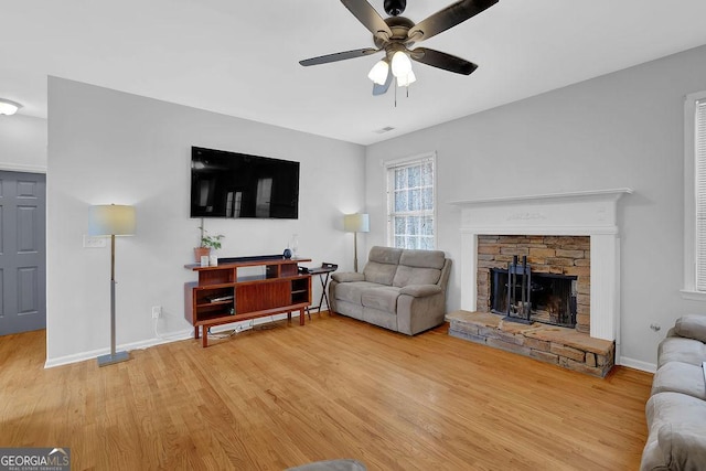 living room with a stone fireplace, hardwood / wood-style floors, and ceiling fan