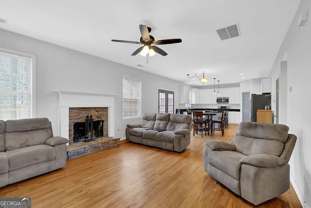 living room with a stone fireplace, light hardwood / wood-style flooring, and ceiling fan