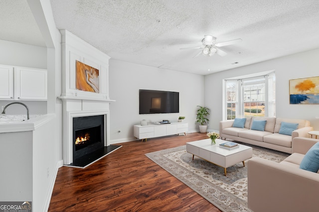 living room featuring ceiling fan, dark wood-type flooring, a large fireplace, and a textured ceiling