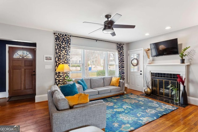 living room with wood-type flooring, a tile fireplace, and ceiling fan