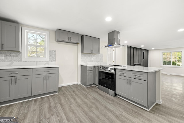 kitchen featuring gray cabinets, stainless steel range with electric stovetop, island range hood, light hardwood / wood-style floors, and kitchen peninsula