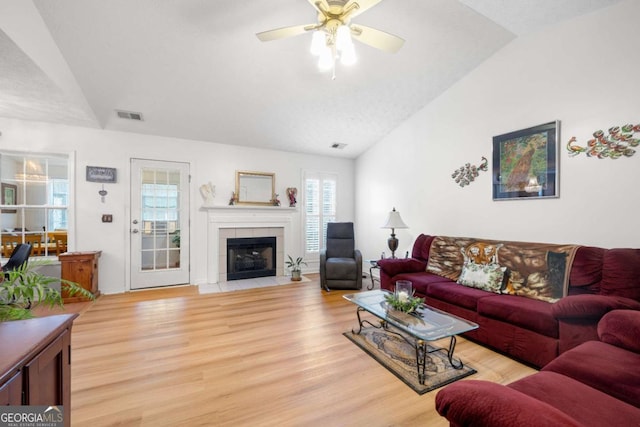 living room featuring ceiling fan, lofted ceiling, a tiled fireplace, and light hardwood / wood-style flooring