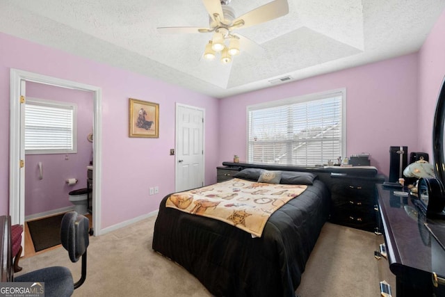 bedroom featuring ceiling fan, a tray ceiling, light colored carpet, and a textured ceiling