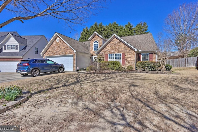 view of front of property featuring an attached garage, fence, stone siding, and driveway