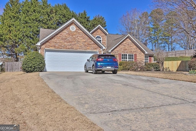 view of front of home with concrete driveway, an attached garage, fence, and stone siding