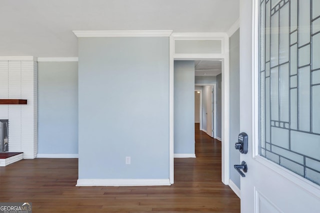 entryway with dark wood-type flooring, crown molding, and a brick fireplace