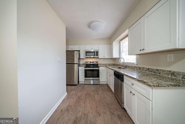 kitchen featuring sink, light hardwood / wood-style flooring, dark stone countertops, appliances with stainless steel finishes, and white cabinets