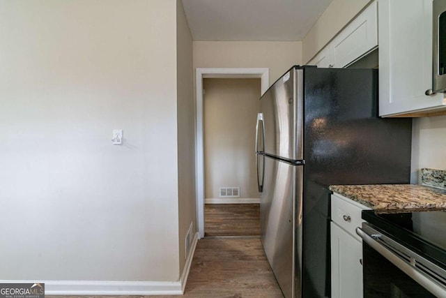 kitchen featuring dark stone countertops, stainless steel appliances, light hardwood / wood-style flooring, and white cabinets