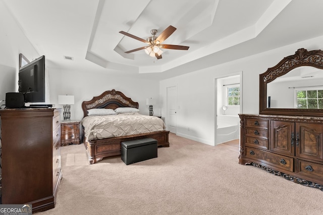 carpeted bedroom with a raised ceiling, ceiling fan, connected bathroom, and multiple windows