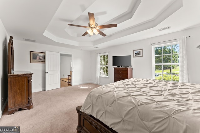 bedroom with light colored carpet, ceiling fan, and a tray ceiling