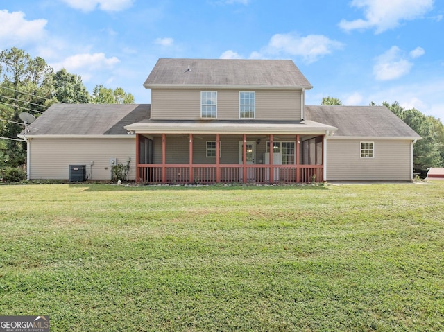 rear view of house with central AC, a sunroom, and a lawn