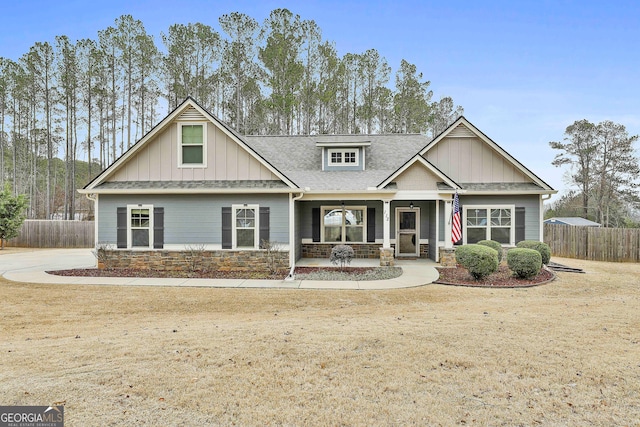 craftsman inspired home featuring a shingled roof, stone siding, covered porch, fence, and board and batten siding