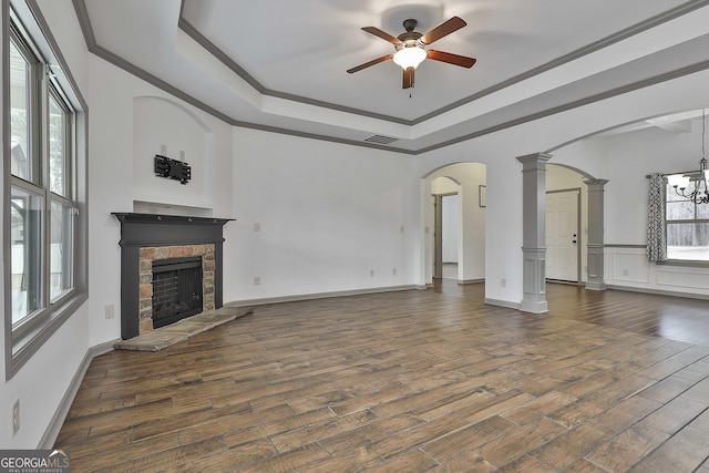 unfurnished living room with dark wood-style floors, arched walkways, a tray ceiling, visible vents, and ornate columns