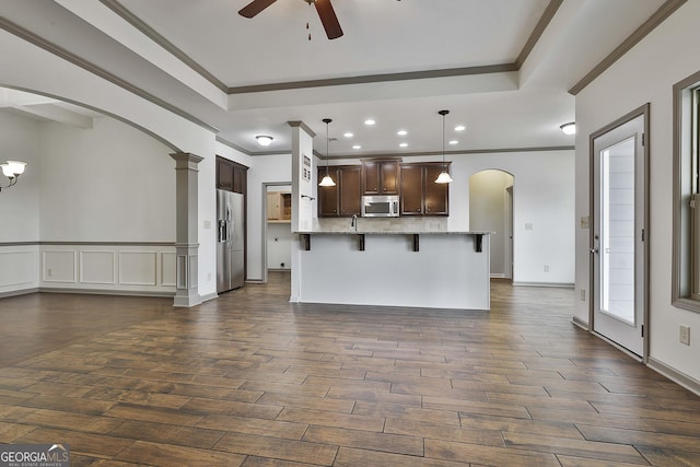 kitchen featuring dark wood-style floors, arched walkways, a breakfast bar, stainless steel appliances, and dark brown cabinetry