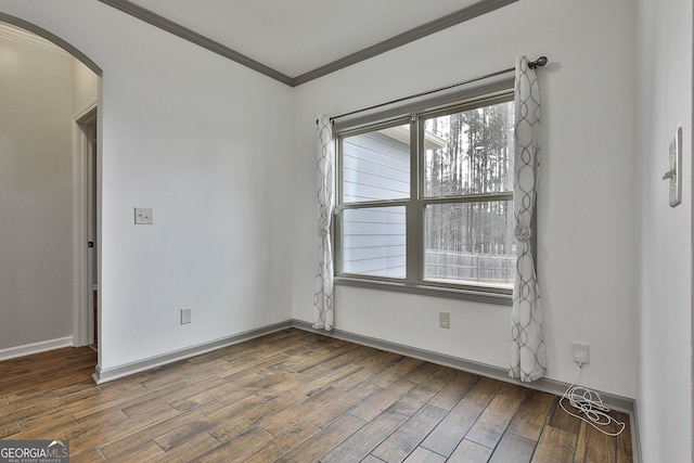 empty room featuring arched walkways, crown molding, baseboards, and wood finished floors