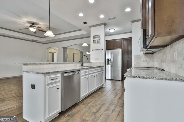 kitchen with arched walkways, dark wood-style flooring, visible vents, appliances with stainless steel finishes, and decorative backsplash