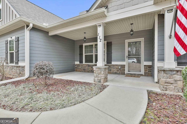 property entrance featuring stone siding, covered porch, board and batten siding, and roof with shingles