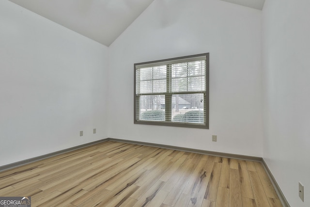 empty room with high vaulted ceiling, light wood finished floors, and baseboards