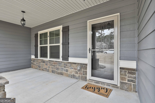 view of exterior entry featuring stone siding and covered porch