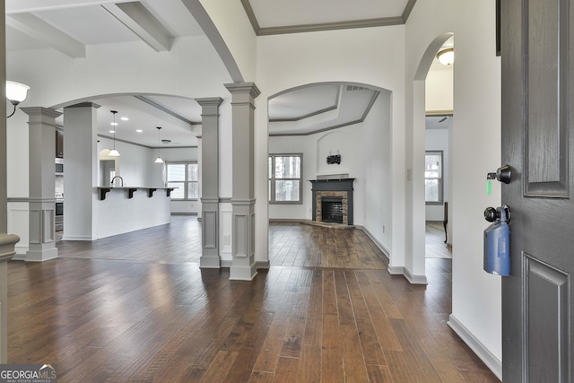 foyer with dark wood-style floors, a stone fireplace, ornamental molding, and ornate columns