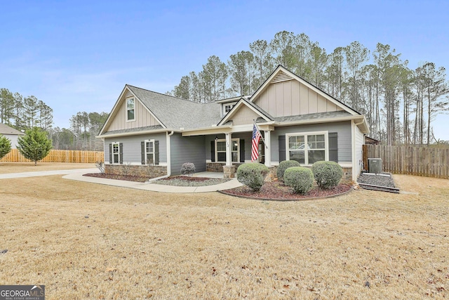 craftsman house with board and batten siding, stone siding, fence, and central air condition unit