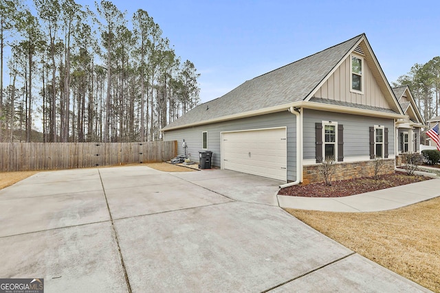 view of property exterior featuring a shingled roof, concrete driveway, board and batten siding, fence, and stone siding