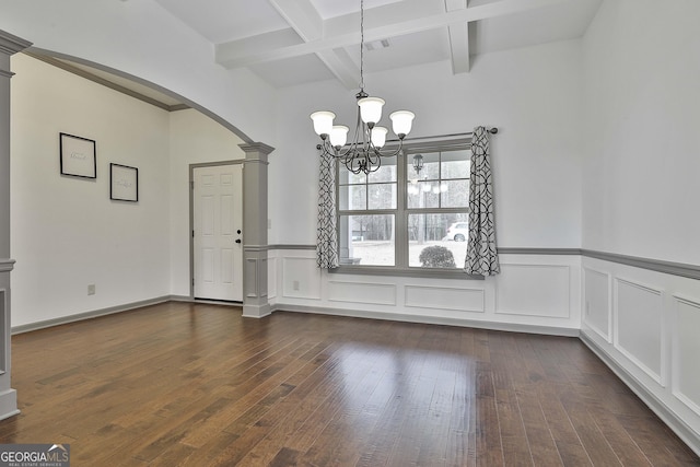 unfurnished dining area with decorative columns, arched walkways, dark wood finished floors, beam ceiling, and a notable chandelier