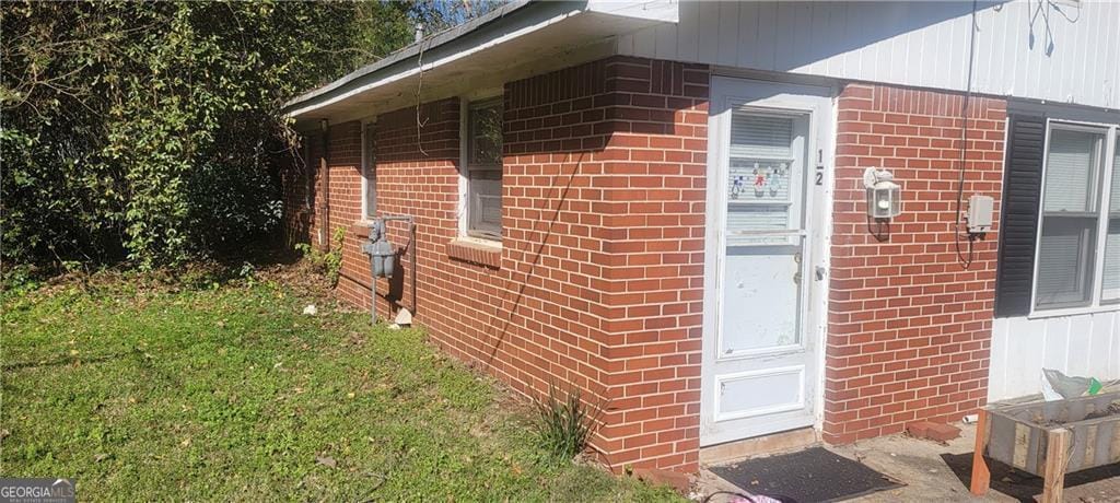 view of exterior entry with brick siding and a lawn