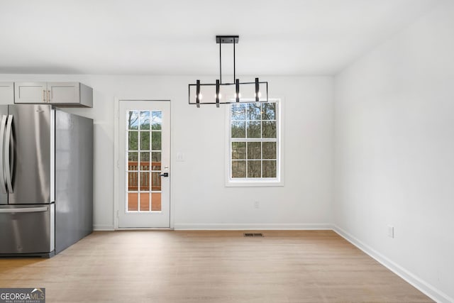 unfurnished dining area with a chandelier and light hardwood / wood-style flooring