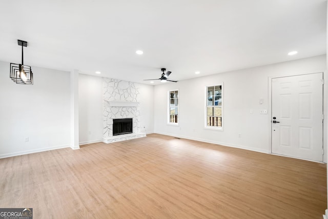 unfurnished living room with ceiling fan, a stone fireplace, and light hardwood / wood-style floors