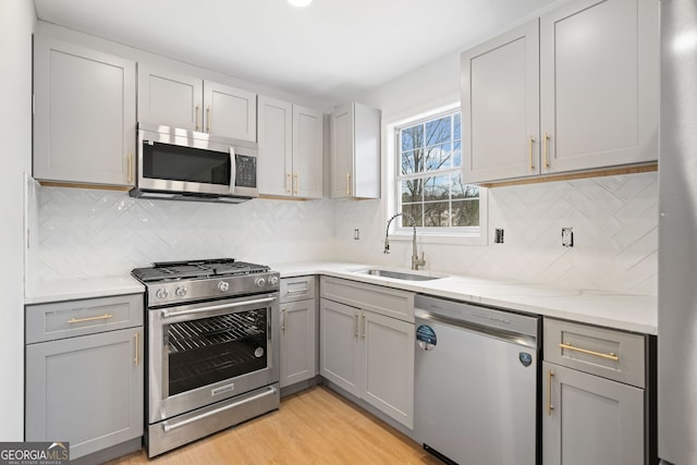 kitchen featuring sink, gray cabinetry, light stone counters, stainless steel appliances, and light hardwood / wood-style floors