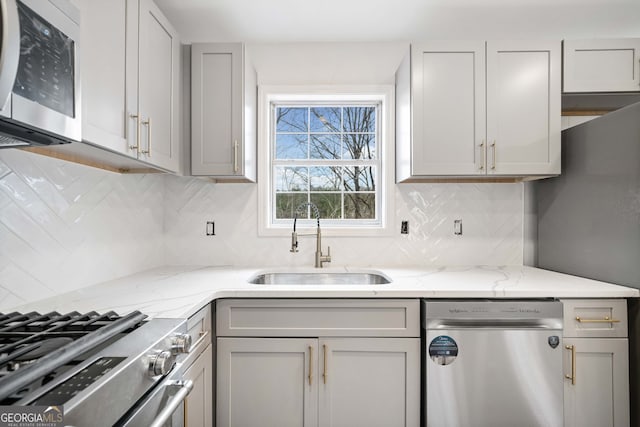 kitchen featuring sink, gray cabinets, backsplash, stainless steel appliances, and light stone counters