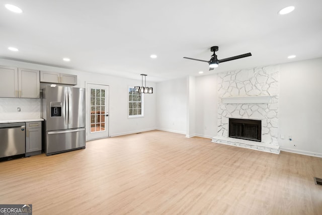 unfurnished living room featuring ceiling fan, a stone fireplace, and light hardwood / wood-style floors