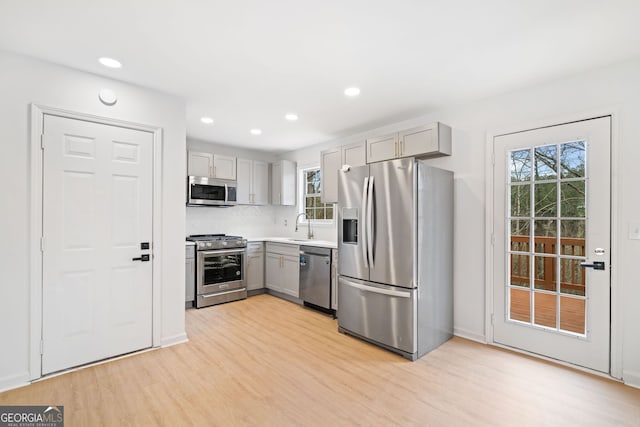 kitchen with gray cabinets, tasteful backsplash, sink, stainless steel appliances, and light wood-type flooring