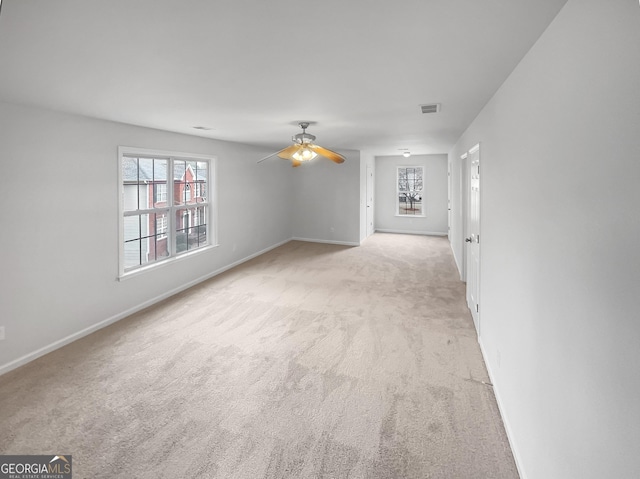 empty room with a wealth of natural light, light colored carpet, and ceiling fan