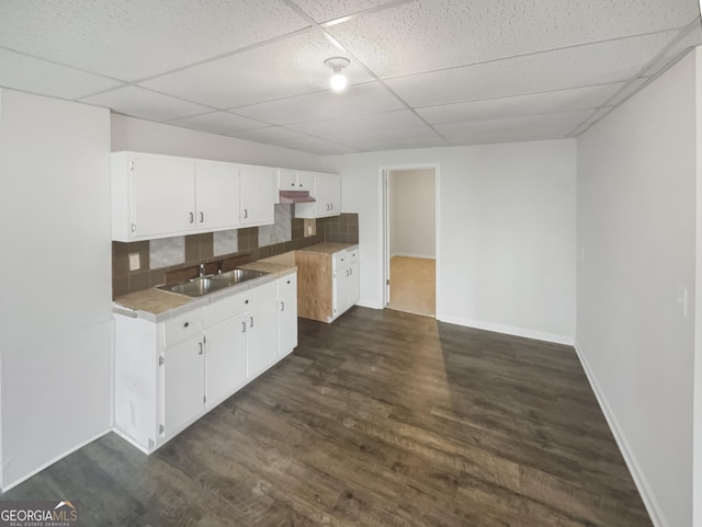 kitchen with sink, dark hardwood / wood-style flooring, white cabinets, decorative backsplash, and a drop ceiling