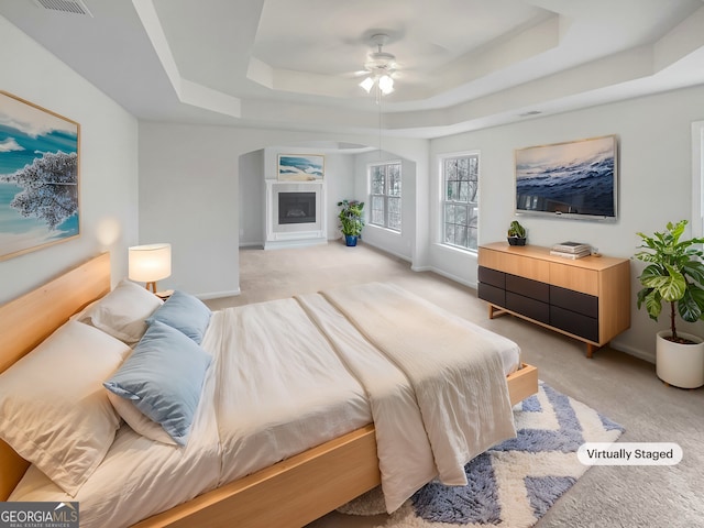 carpeted bedroom with ceiling fan and a tray ceiling